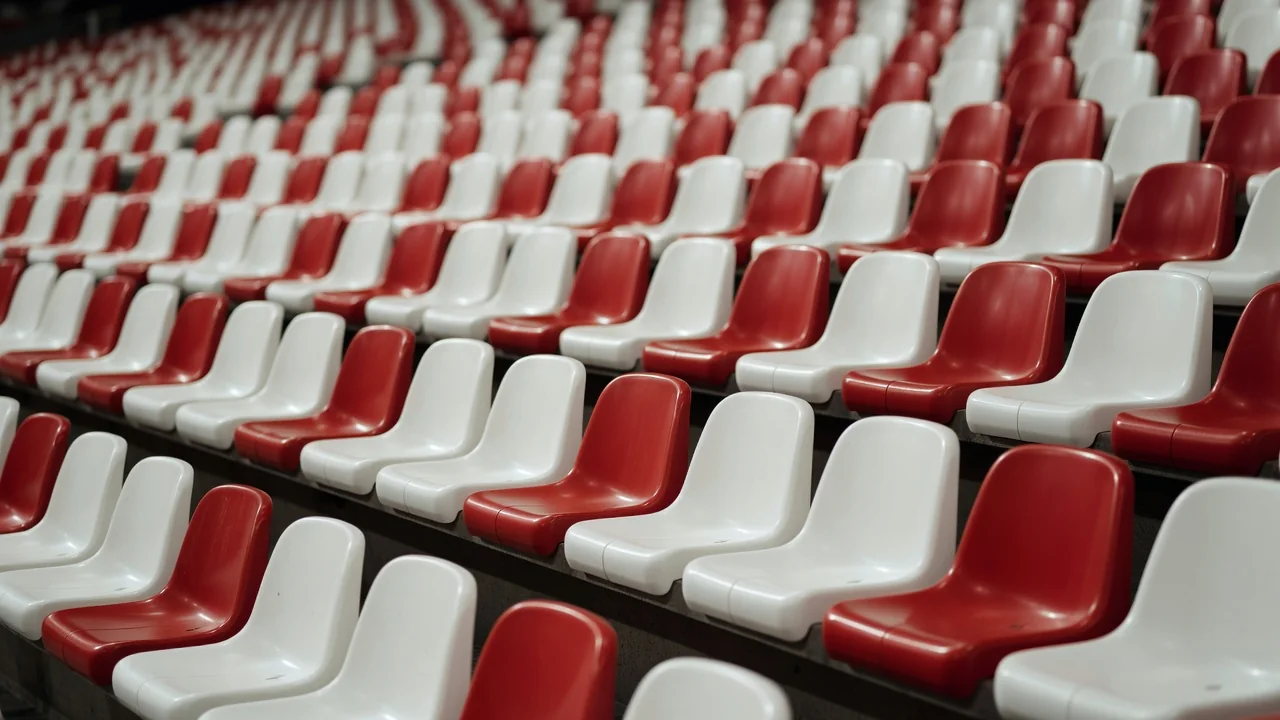 Filas de asientos rojos y blancos vacíos en las gradas de un estadio.