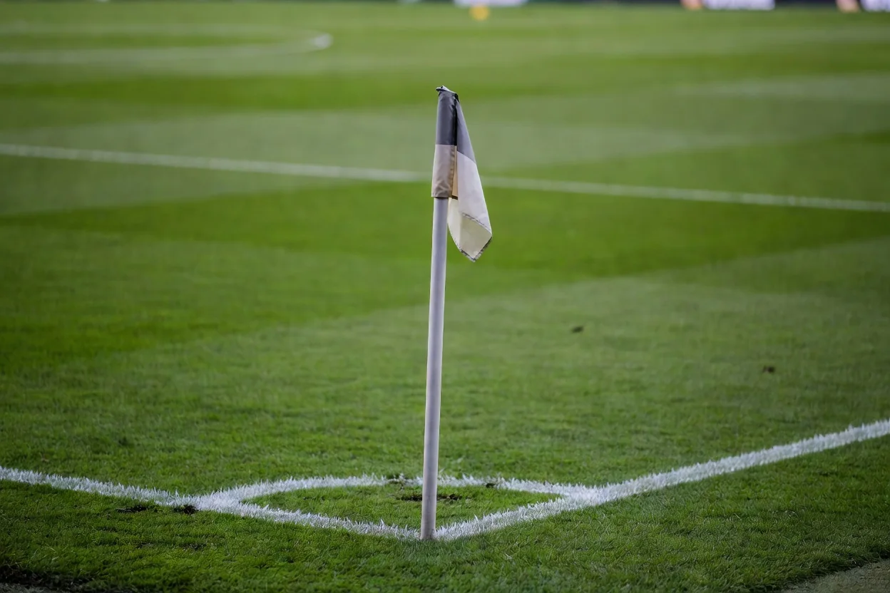 Un banderín de córner clavado en el césped con las líneas del campo desenfocadas.